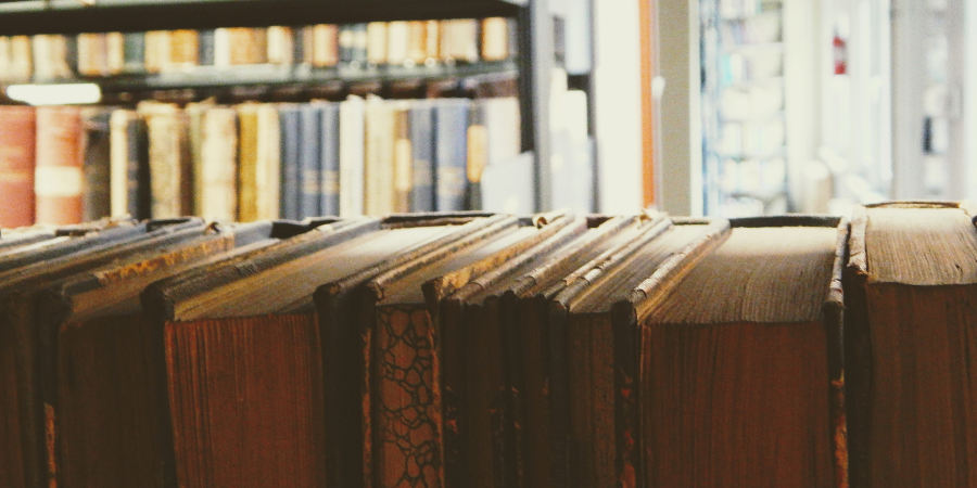 Regały biblioteczne widoczne zza grzbietów książek stojących na półce.