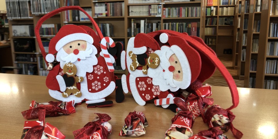 Dwa koszyczki w kształcie Świętego Mikołaja na blacie w Wypożyczalni wokół których leżą cukierki.
