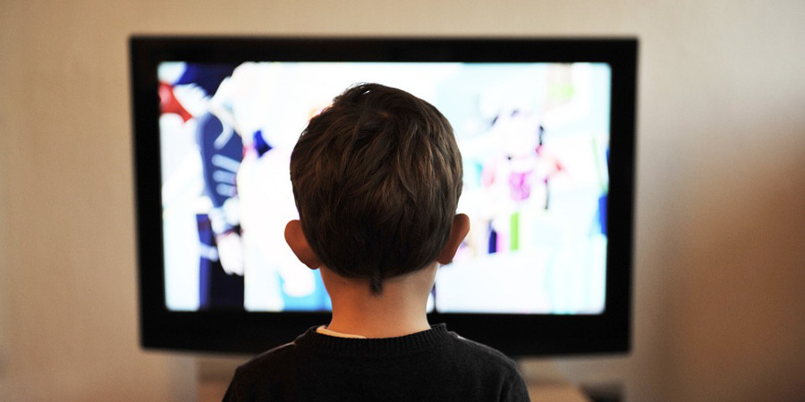 Widoczna od tyłu głowa chłopca wpatrującego się w odbiornik telewizyjny.