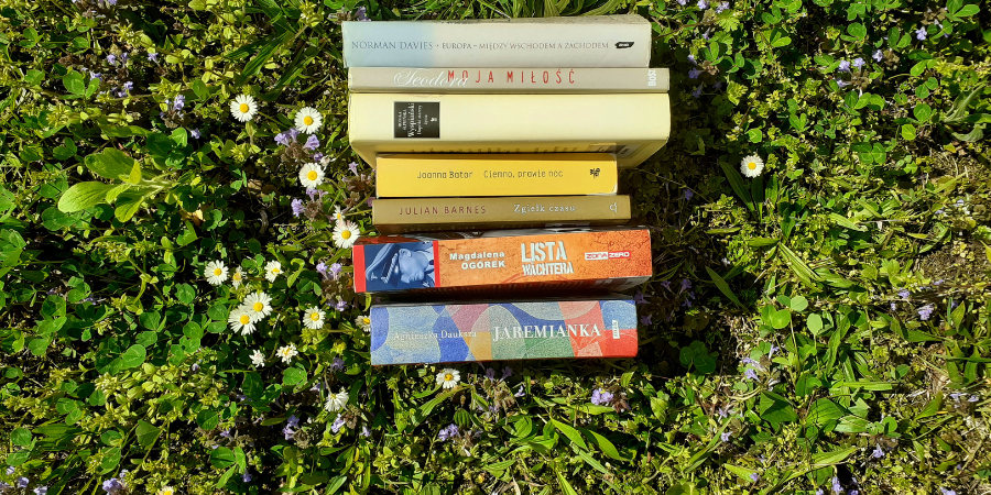 Książki z literatury pięknej ułożone grzbietami na zielonej trawie, wśród kwiatów