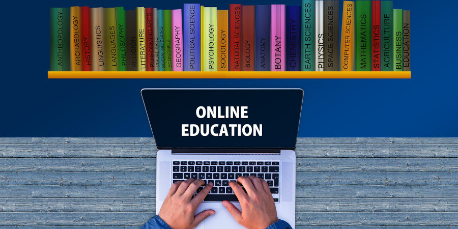 Dłonie piszące na klawiaturze laptopa, na ekranie napis online education, na ścianie półka z podręcznikami z różnych dziedzin