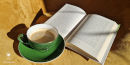 Na żółtym fotelu zielona filiżanka z kawą oraz otwarta książka.