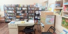 Na pierwszym planie biurko z ułożonymi materiałami, obok kartkowy katalog biblioteczny. W tle półki z książkami.
