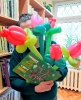 Kobieta w zielonym swetrze na tle regałów z książkami trzyma róże wykonane z balonów i zieloną książkę pt. 'Wiosna'