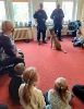 Dwoje policjantów i pies policyjny stoją przed grupą dzieci.