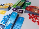 Widok z góry na rozłożone na stole elementy gry FITS, tj. 4 plastikowe rampy częściowo zakryte różnokształtnymi kafelkami w kolorach graczy