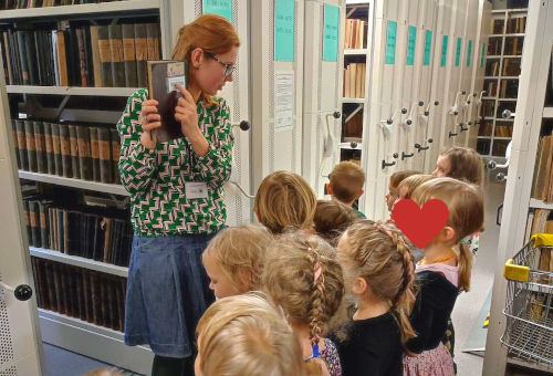 Kobieta pokazuje grupce dzieci książkę w magazynie z książkami.