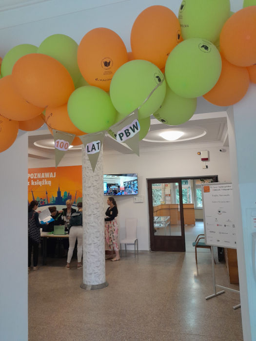 Wejście do Biblioteki ozdabia girlanda z zielonych i pomarańczowych balonów, widok na hol i rejestrację konferencji