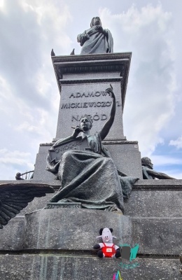 Pluszowy Koziołek Klemens siedzi pod pomnikiem Adama Mickiewicza na krakowskim Rynku