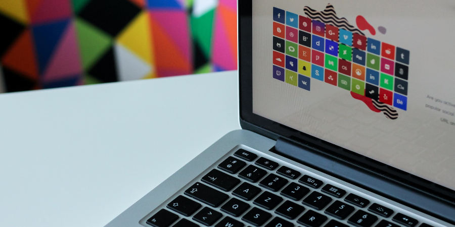 Na jasnym blacie biurka otwarty laptop z yświetlonymi kolorowymi ikonkami w programie graficznym