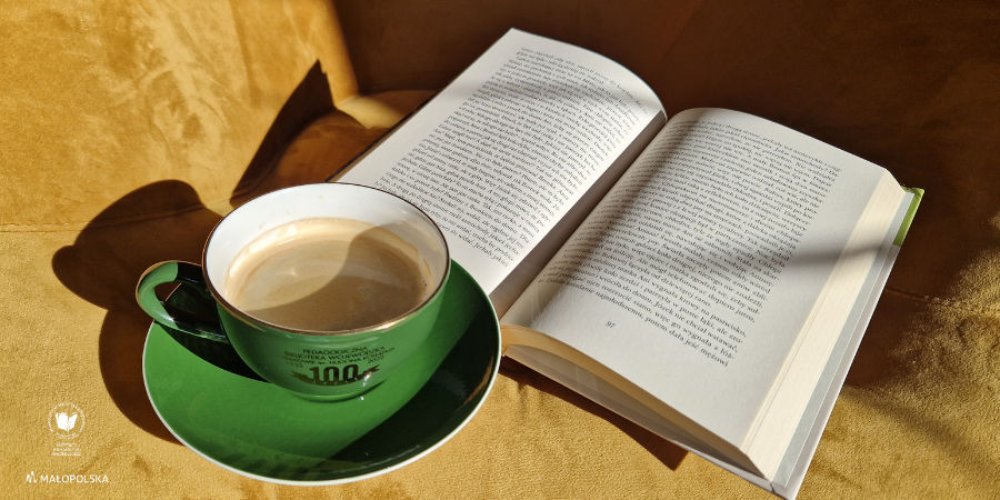 Na żółtym fotelu zielona filiżanka z kawą oraz otwarta książka.