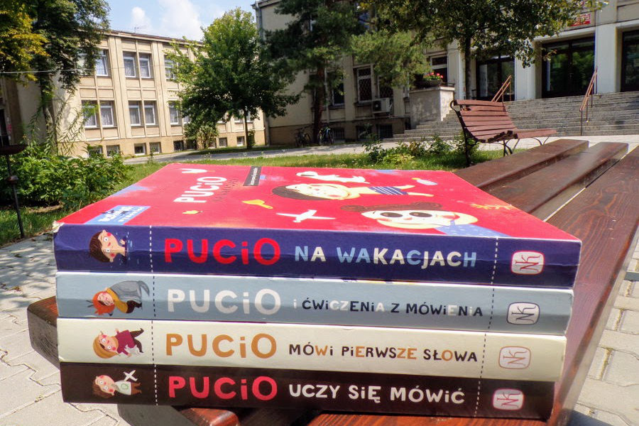 Cztery książeczki dla dzieci z serii o przygodach Pucia na ławce przed budynkiem biblioteki.