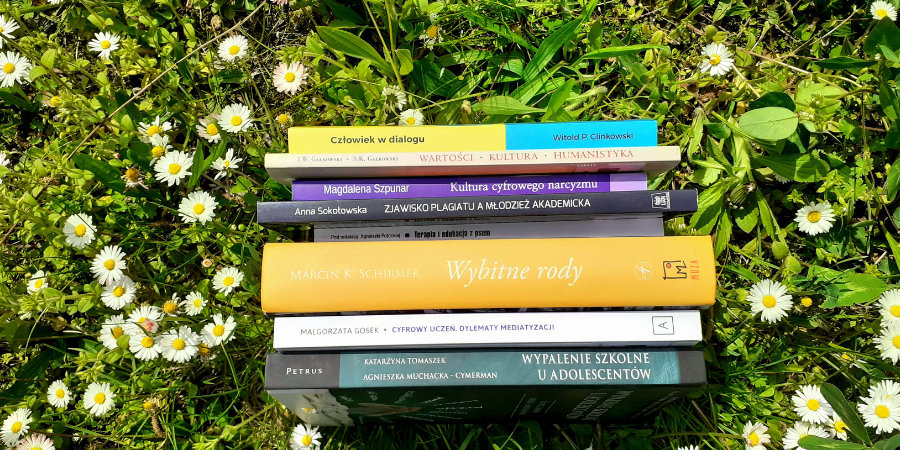 Książki z literatury fachowej ułożone grzbietami na zielonej trawie, wśród kwiatów