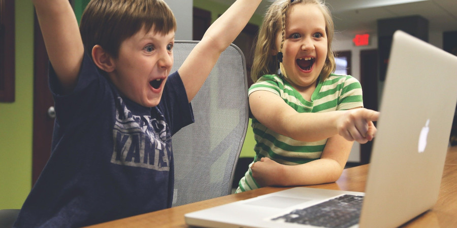 Roześmiany chłopiec z rękoma uniesionymi do góry i dziewczynka wskazująca entuzjastycznie na ekran laptopa