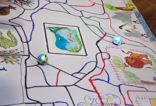 Na białej kartce narysowane kolorowe trasy, zwierzęta oraz staw. Po trasach poruszają się roboty Ozoboty. 