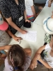 Prowadząca warsztaty zapisuje na kartce papieru historię, wokół stołu stoją dzieci