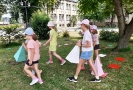 Grupka dziewczyn na trawie przed Biblioteką niesie kolorowe stożki - elementy gry wielkoformatowej