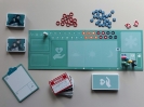 Widok z góry na rozłożone na stole elementy gry Ostatnie chwile, tj. plansza do gry, na niej różnokolorowe pionki lekarzy i pielęgniarek, karty narracji i żetony funkcyjne