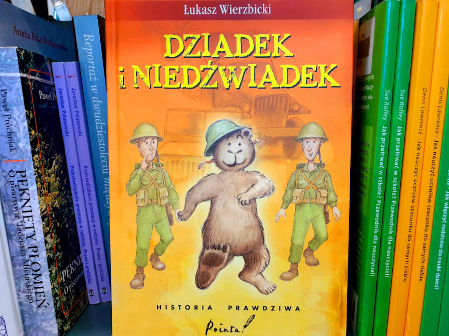 Front okładki książki "Dziadek i Niedźwiadek" na półce z różnokolorowymi książkami stojącymi grzbietem