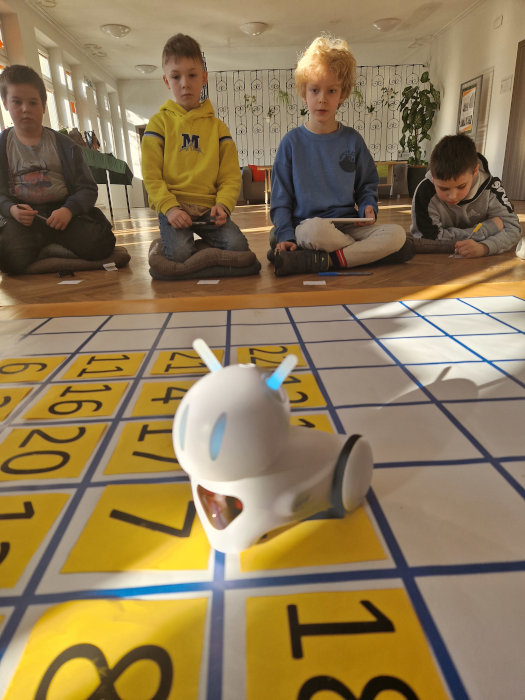 Chłopiec z tabletem programuje robota Photona, który stoi na żółtym karteczkach z cyframi