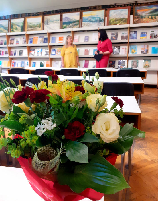 Na pierwszym planie kolorowy bukiet kwiatów, w tle Pani Dyrektor Anna Piotrowska rozmawia z Panią Dorotą Ferens