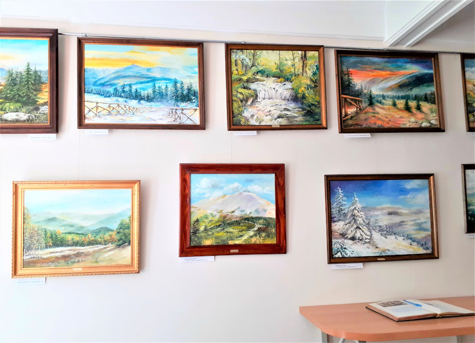Obrazy wiszące na ścianie w Wypożyczalni, na stoliku otwarta księga pamiątkowa z wernisażu wystawy