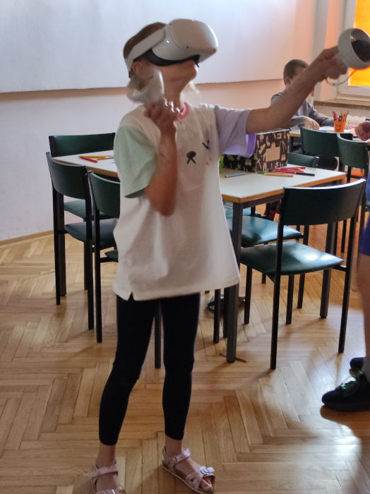 Dziewczynka z gogalmi Oculus Quest 2 założonymi na głowę, w rękach trzymająca joystiki do sterowania