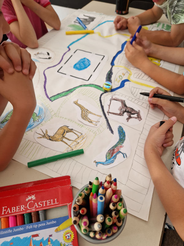 Grupa dzieci rysujących kolorowe trasy dla robota w okół narysowanej makiety ZOO.  