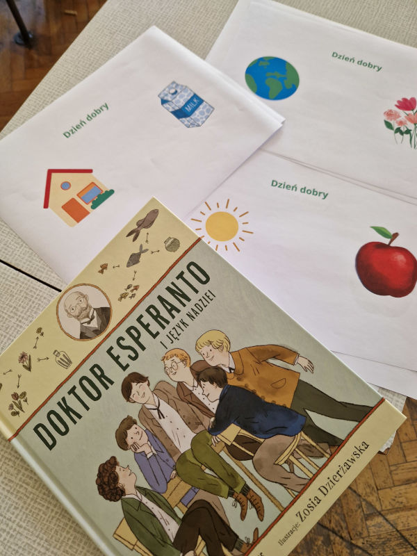 Na stoliku leży książka "Doktor Esperanto i język nadziei" oraz kartki z zadaniami.