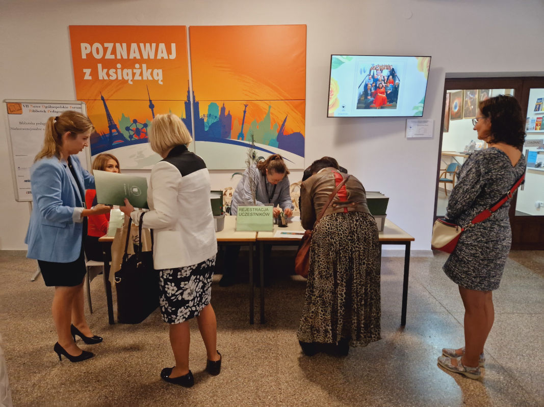 Trzy kobiety w kolejce do rejestracji na konferencję. Stoją przy stoliku z napisem "Rejestracja uczestników".