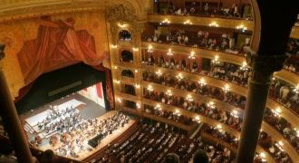 Zdjęcie Złoto-purpurowe wnętrze klasycznego teatru. Po bokach 6 pięter lóż, na dole pod kurtyną widać orkiestron.